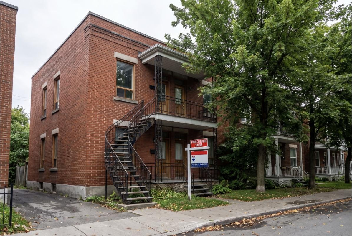 Montreal duplex with a for sale sign and a foreclosure rider sign